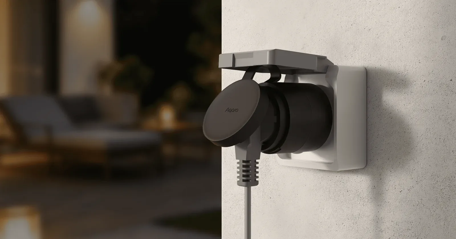 Black Aqara Outdoor Plug H2 EU plugged into a lidded outdoor wall socket next to a patio at dusk